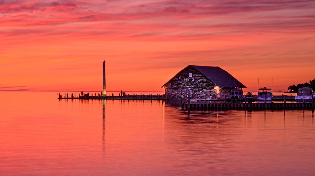 Un tramonto su una superficie d'acqua calma con un molo e un edificio con tetto a forma di piramide.