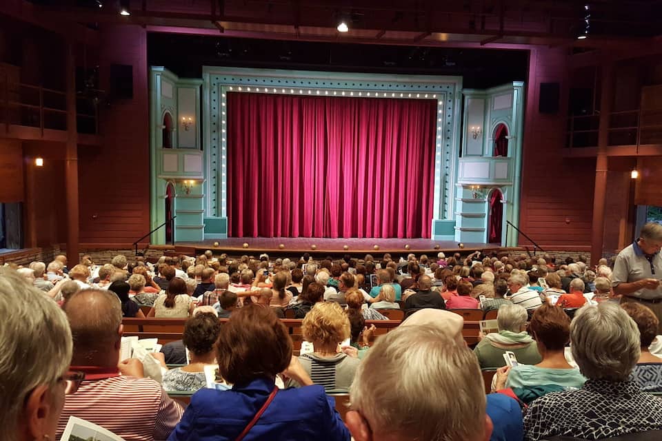 A theater with a stage, red curtains, and a seated audience.
