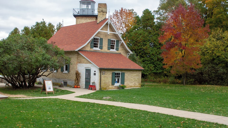 A historic stone building with a red roof and a lighthouse on top, surrounded by a grassy area and trees with autumn foliage.