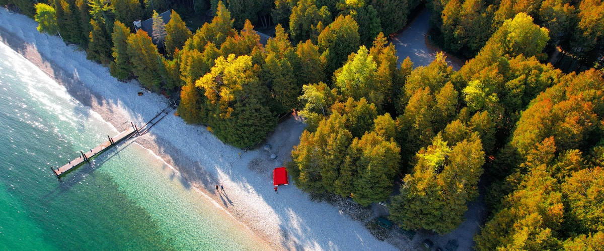 An aerial view of a beach with clear turquoise waters, a wooden pier, and a red structure on the shore.
