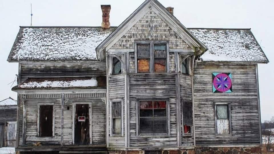 A two-story wooden house with a snow-covered roof and a colorful window sticker.
