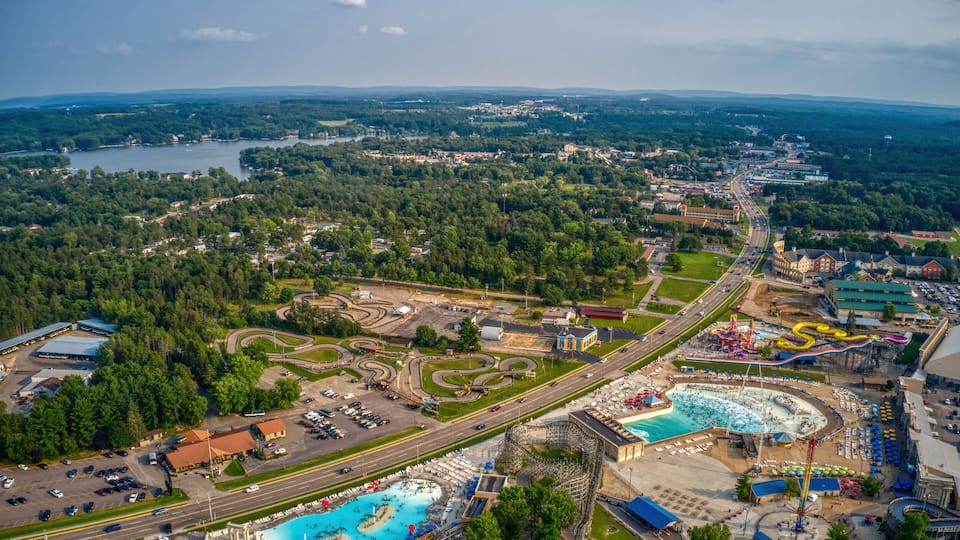 An aerial view of a theme park with roller coasters, a large pool, and surrounding greenery.
