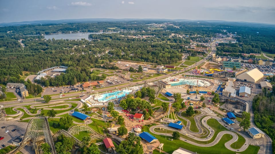 An aerial view of a theme park with roller coasters, a large swimming pool, and surrounding greenery.