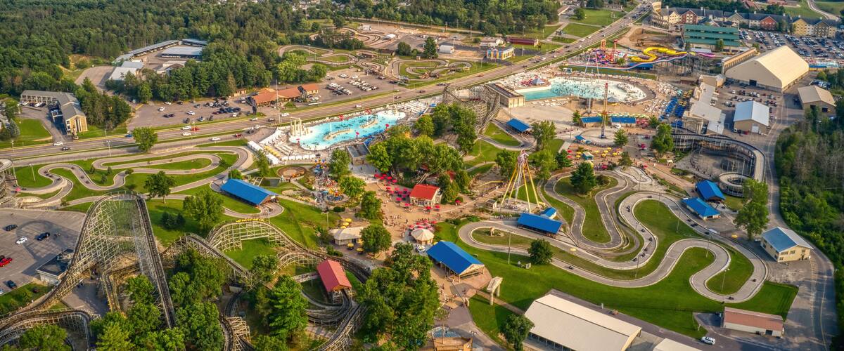 An aerial view of a theme park with roller coasters, a large swimming pool, and surrounding greenery.