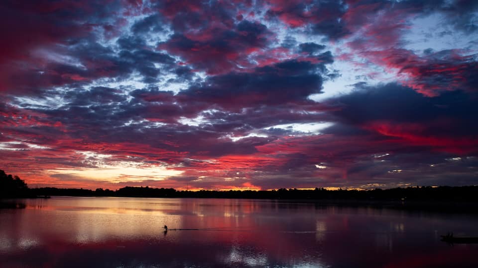 A sunset over a calm lake with vibrant red and purple clouds.