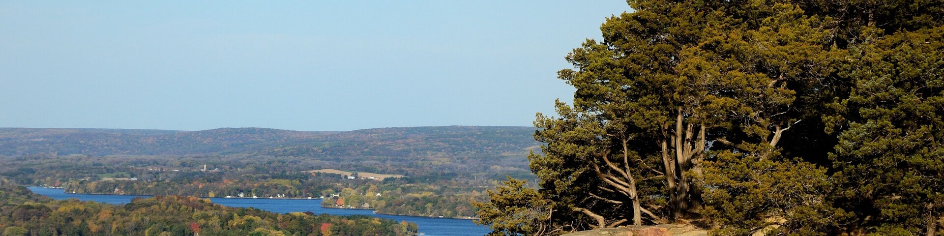 A rocky cliff with trees, a lake, and a distant town.