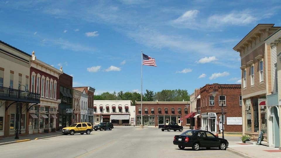 A street with vintage buildings, a flag, and parked cars.