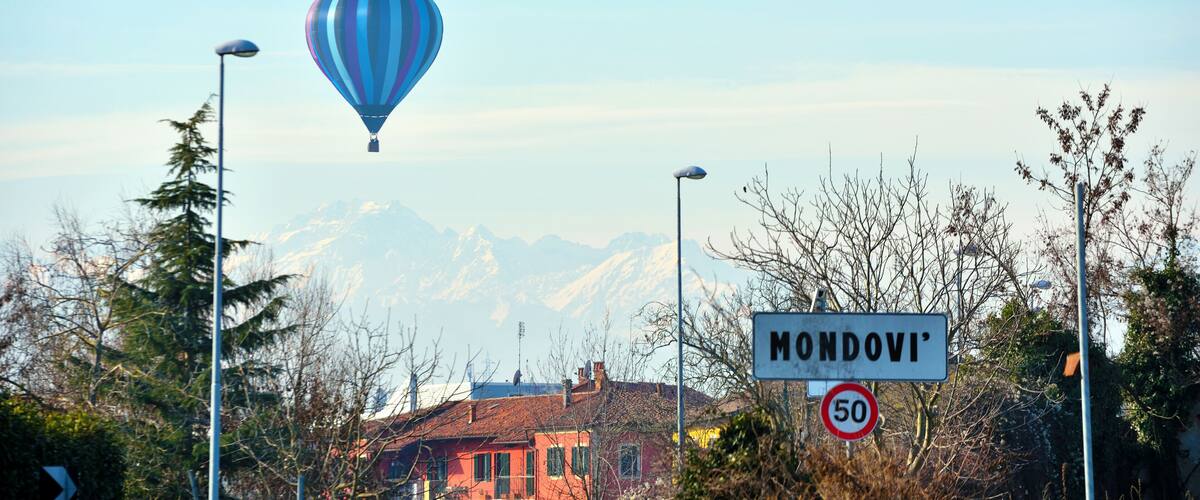 A hot air balloon, a speed limit sign, and a sign reading 'MONDOVI' with a mountain range in the background.