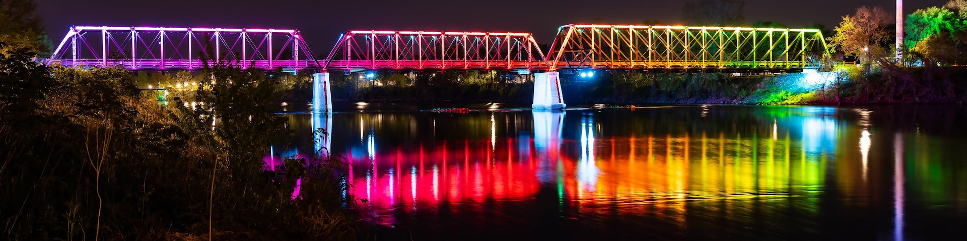 Un puente iluminado con luces de colores que se reflejan en el agua.