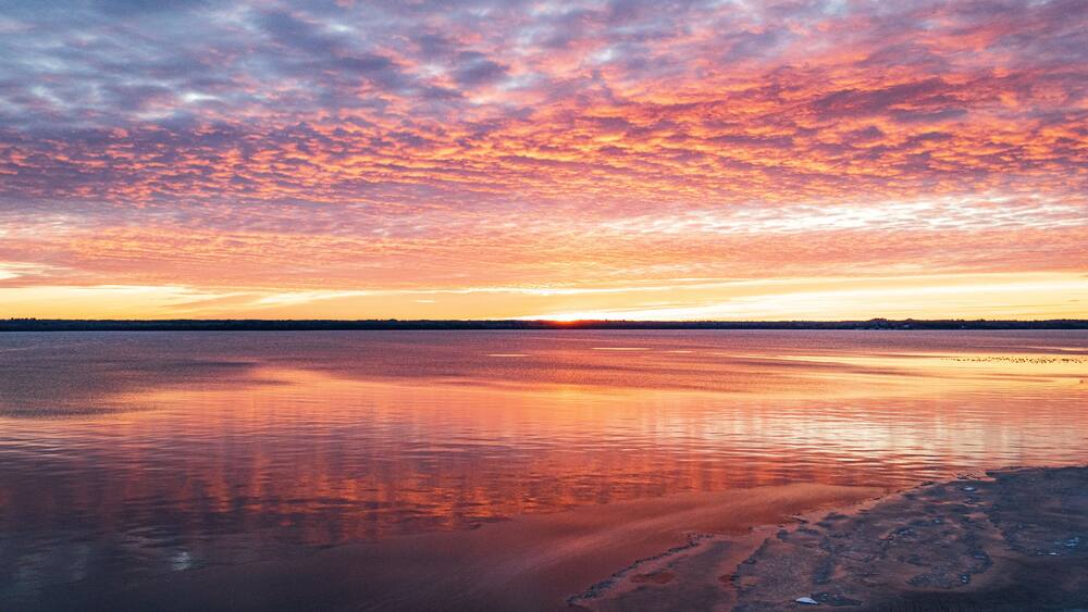 A sunset over a calm lake with a rocky shoreline.