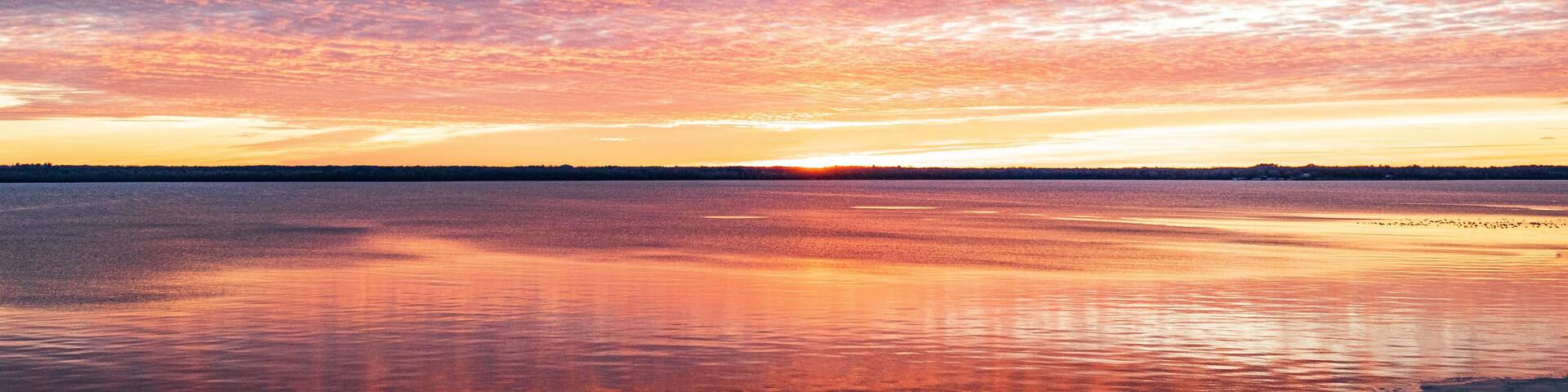 A sunset over a calm lake with a rocky shoreline.