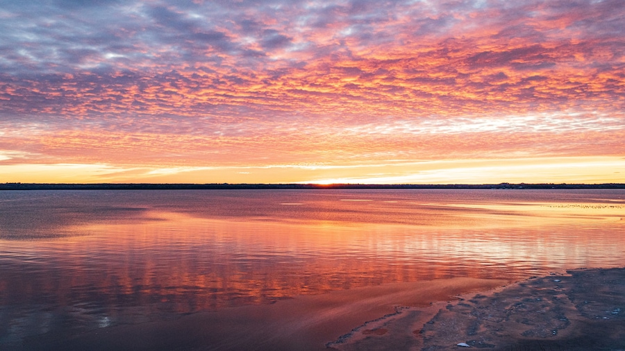 Een zonsondergang boven een kalm meer met een rotsachtige oever.