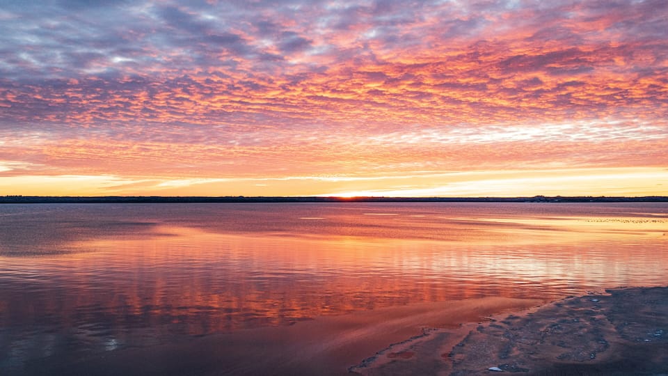 A sunset over a calm lake with a rocky shoreline.