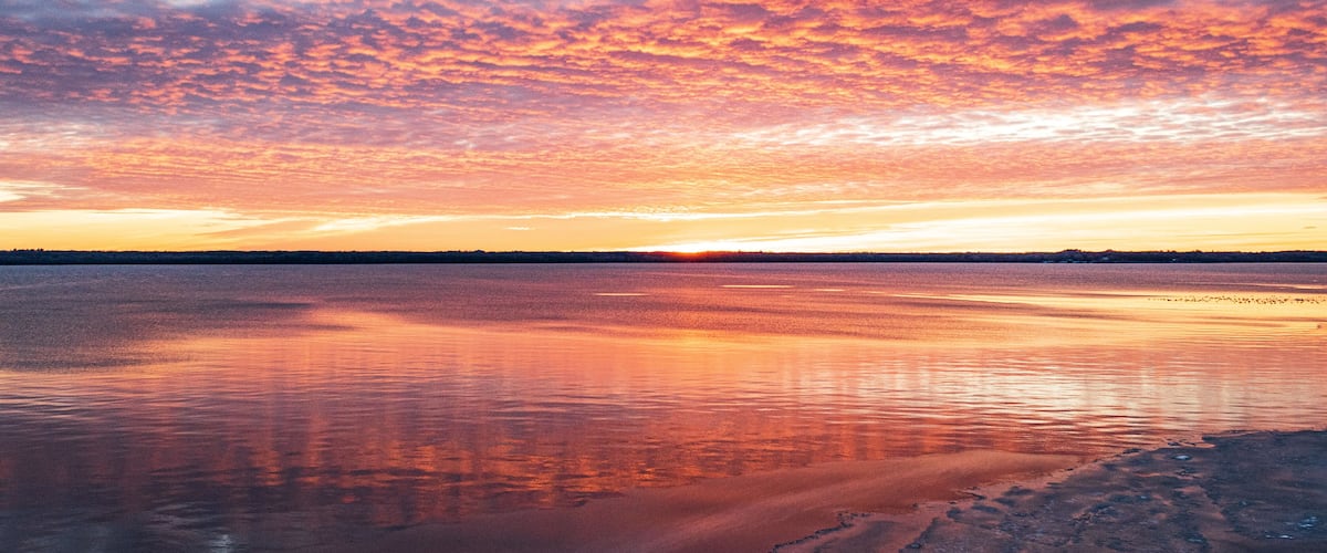 A sunset over a calm lake with a rocky shoreline.