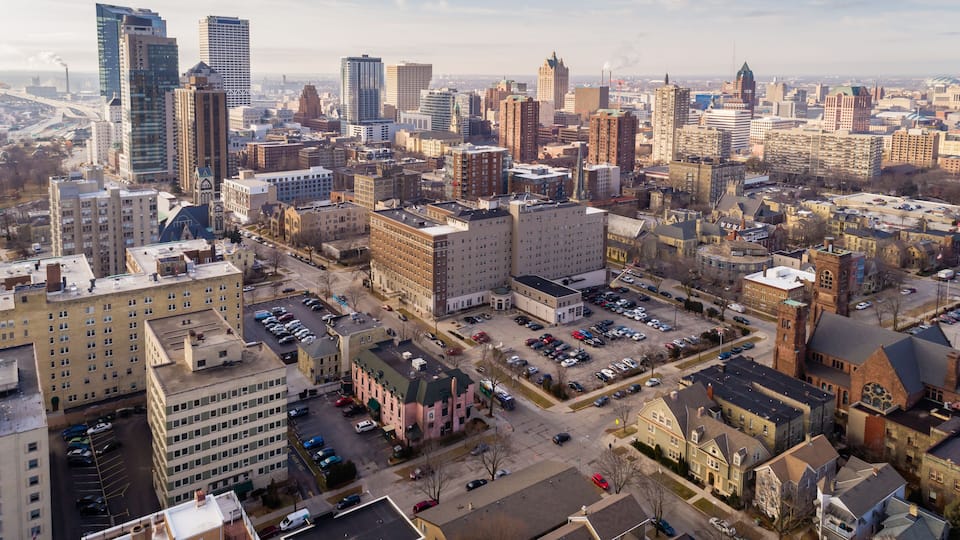 A cityscape with a mix of modern and historic buildings, a large parking lot, and a river in the background.
