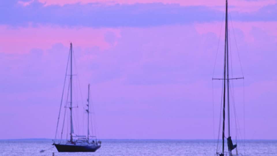 Two sailboats on calm waters with a pink and purple sky.