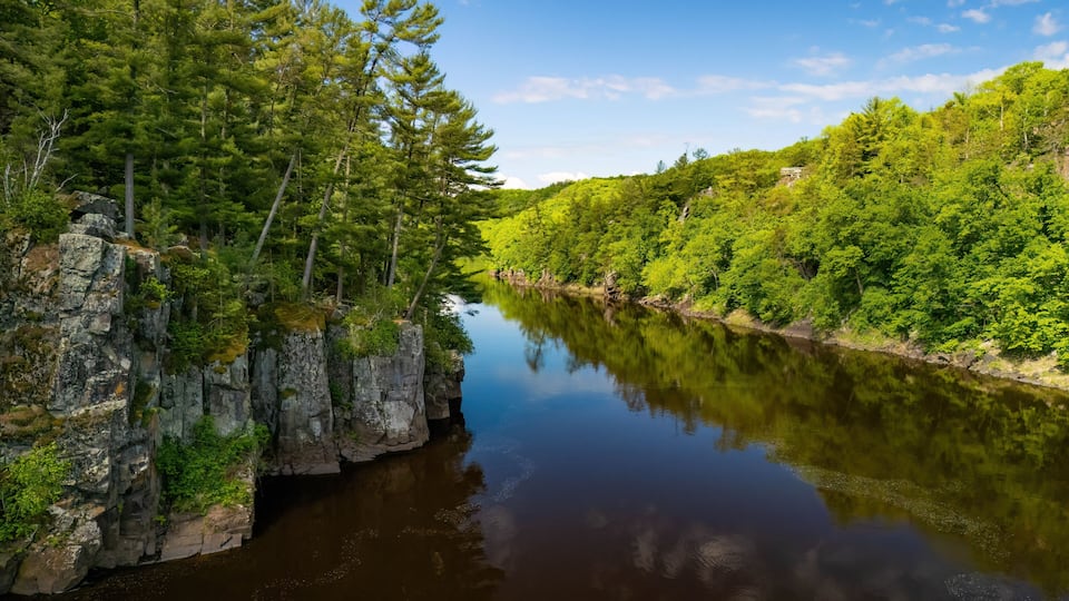 A calm river with rocky cliffs and dense green forest on both sides.