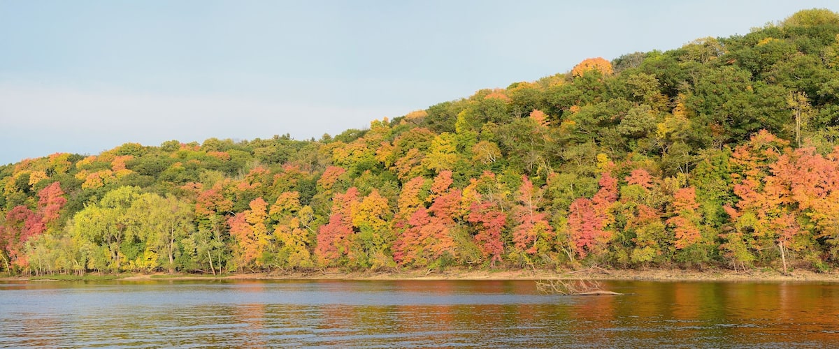 A river with a forested hillside in autumn colors.