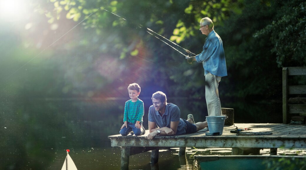 Boy fishing playing with toy sailboat with father grandfather at lake