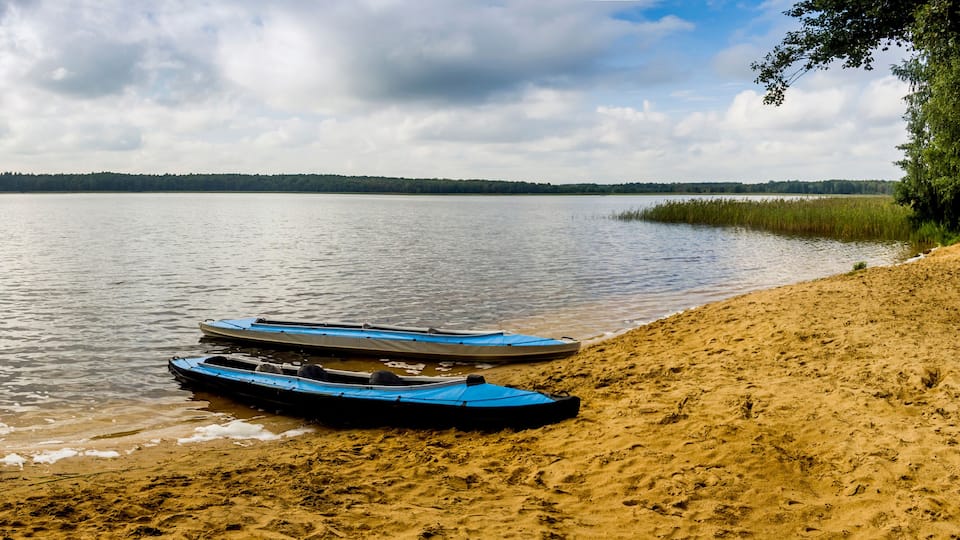A calm lake with kayaks on the shore and a forest in the background.
