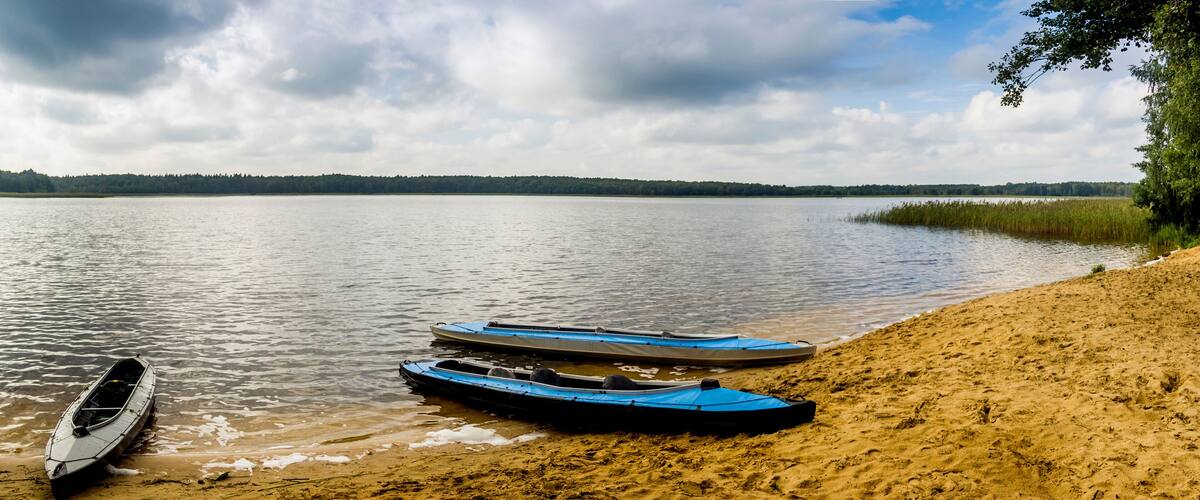 A calm lake with kayaks on the shore and a forest in the background.