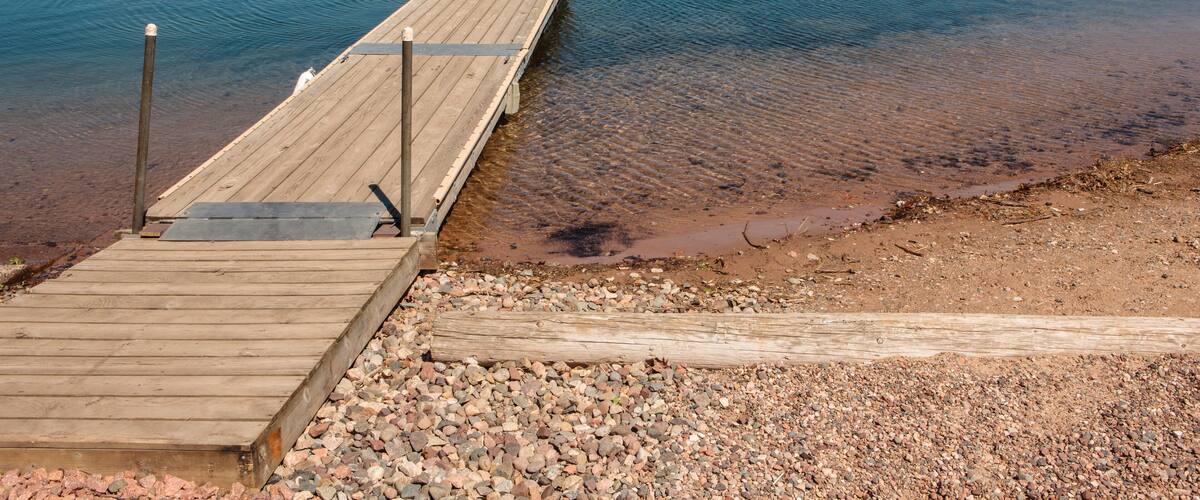 A wooden dock extending into a calm lake with a forest in the background.