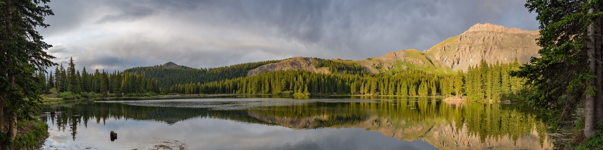 A calm lake surrounded by dense forest and mountains under a cloudy sky.