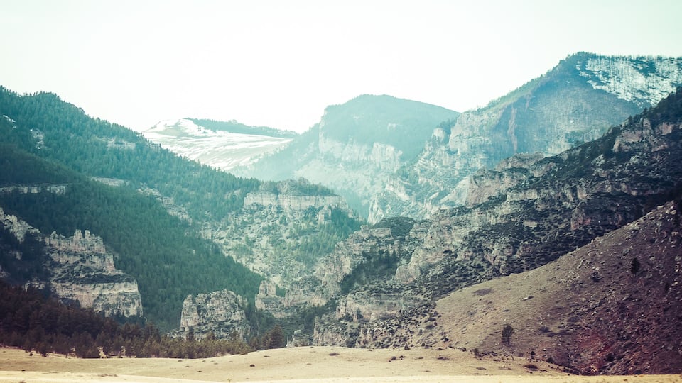 A mountainous landscape with a valley, rocky cliffs, and dense forests.