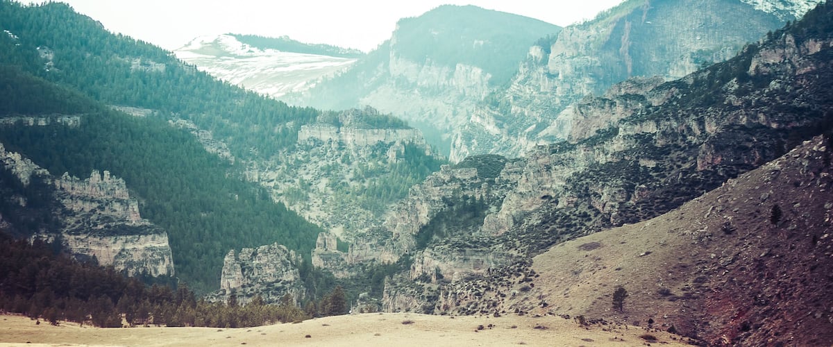 A mountainous landscape with a valley, rocky cliffs, and dense forests.