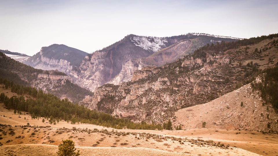 A mountainous landscape with a valley, rocky cliffs, and sparse vegetation.