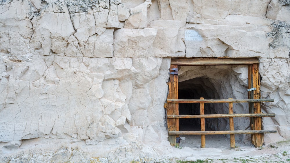 Eingang einer Höhle mit einer Holzleiter und Inschriften an der Felswand.