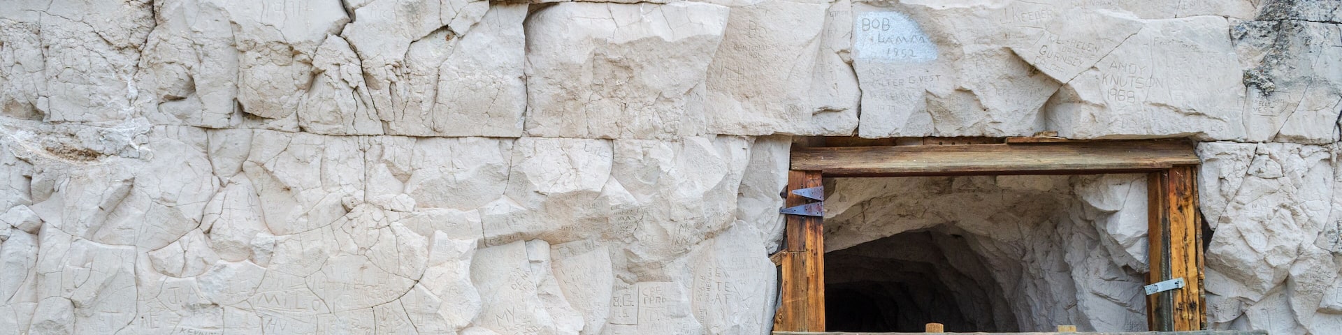 A cave entrance with a wooden ladder and inscriptions on the rock wall.