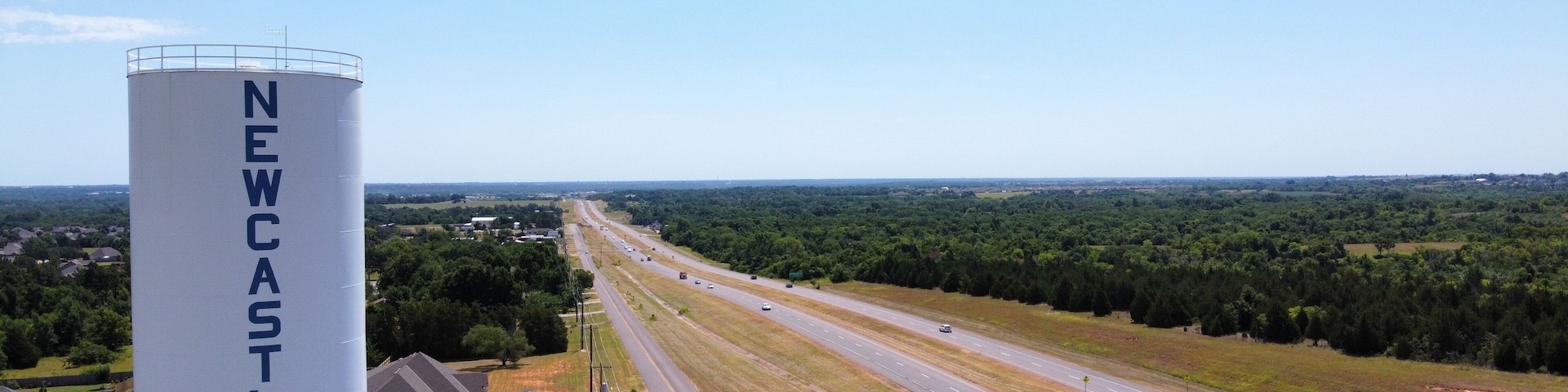 Una autopista con varios carriles, rodeada de vegetación y una estructura cilíndrica blanca destacada con la leyenda 'NEWCASTLE'.