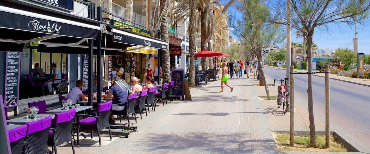 Outdoor cafes with purple chairs and tables, palm trees, and a street with people walking.