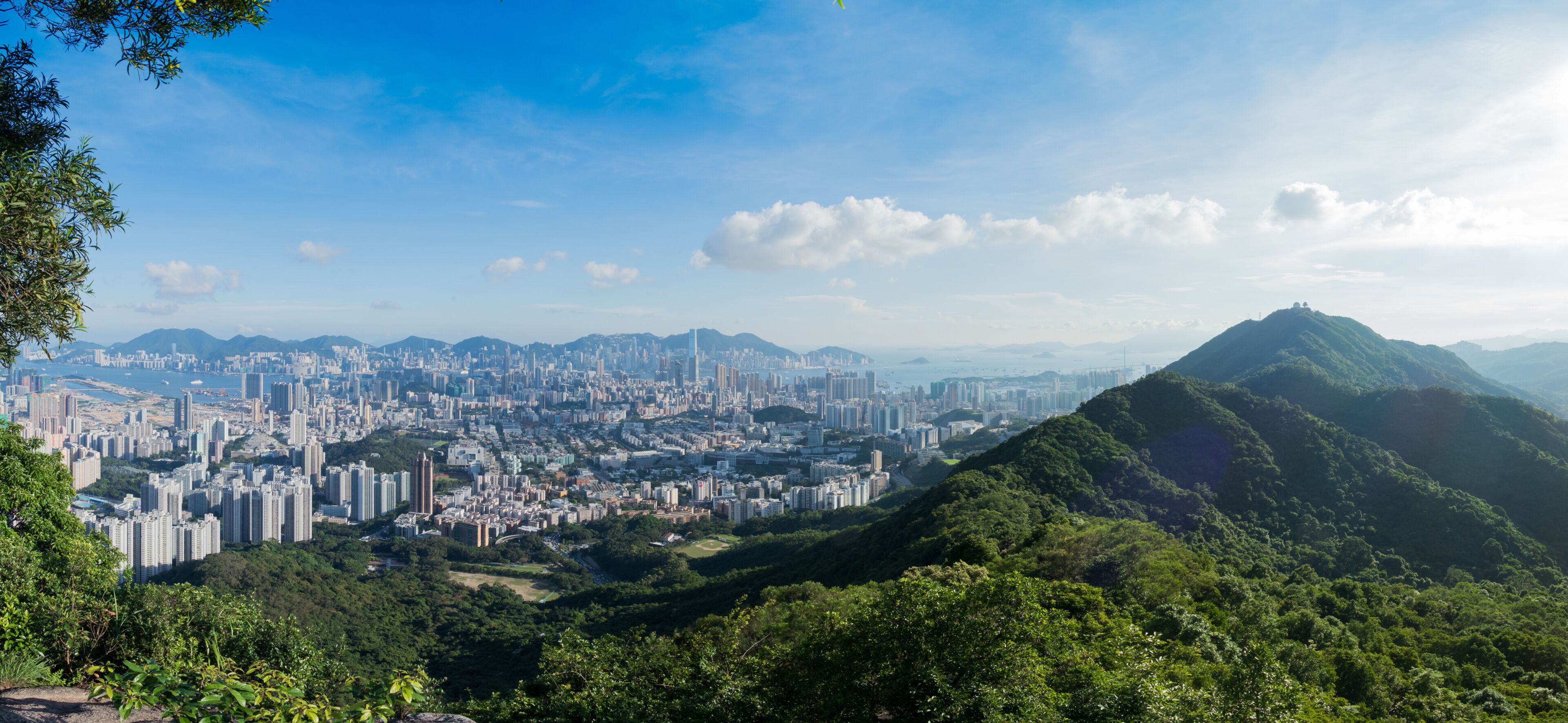 Paisagem urbana com área densa, uma colina proeminente e montanhas distantes sob um céu claro.
