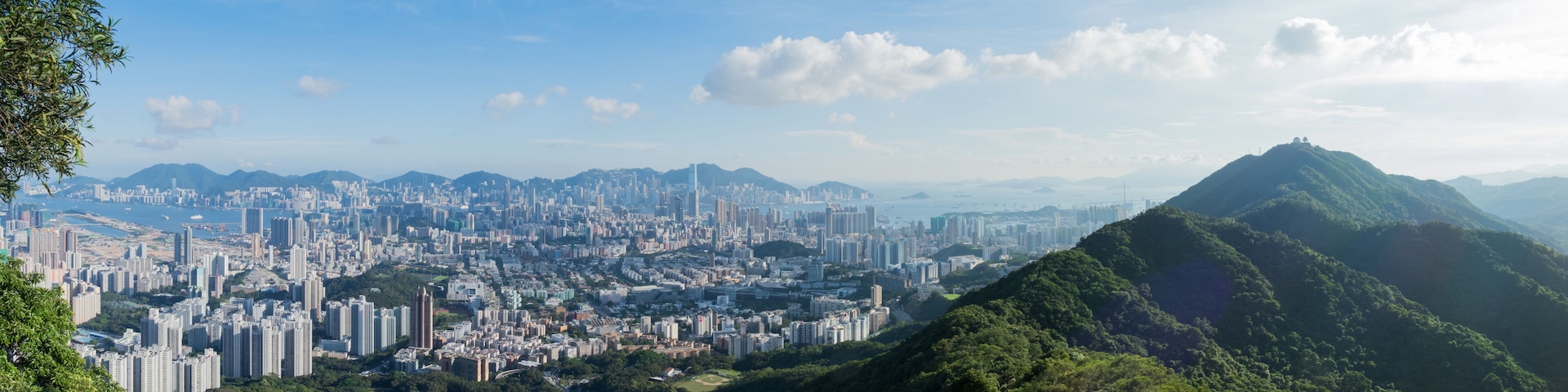 Paisagem urbana com área densa, uma colina proeminente e montanhas distantes sob um céu claro.