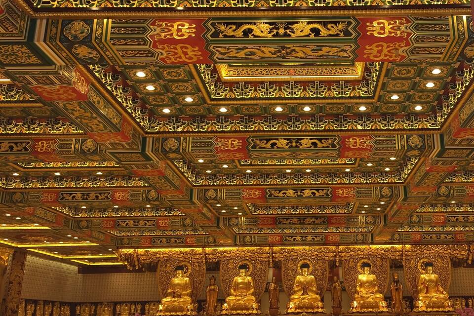 A richly decorated temple interior with ornate golden ceilings and golden statues.