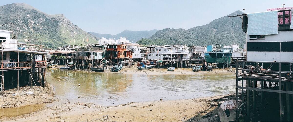 A riverside settlement with buildings and boats, surrounded by mountains.