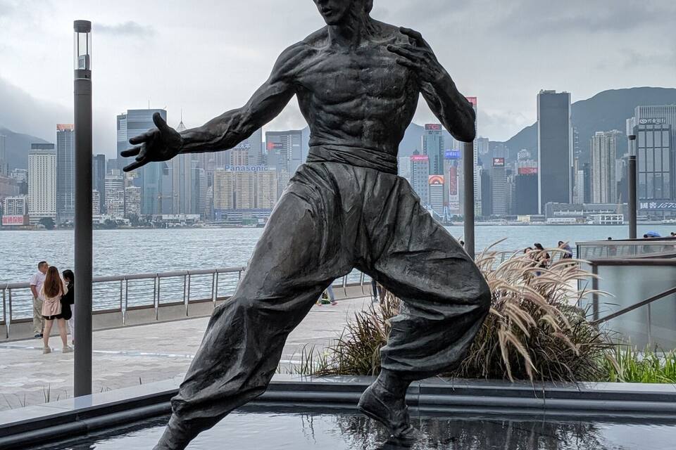 A statue of a muscular figure in a fighting stance, with a city skyline and water in the background.