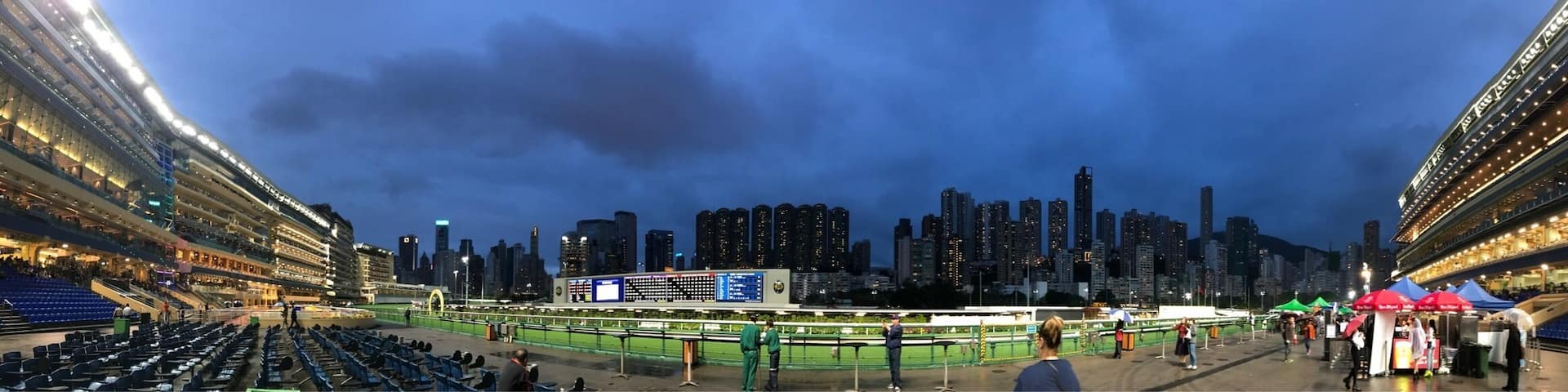 A stadium with a large digital display, surrounded by tall buildings and a city skyline at dusk.