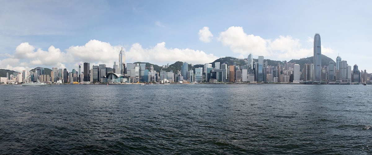 A city skyline with numerous high-rise buildings and a body of water in the foreground.