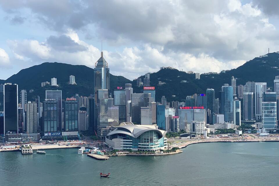 A city skyline with modern skyscrapers, a prominent curved building, and a body of water with boats.