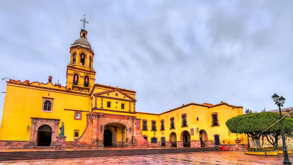 A yellow church with a bell tower and a cross on top.
