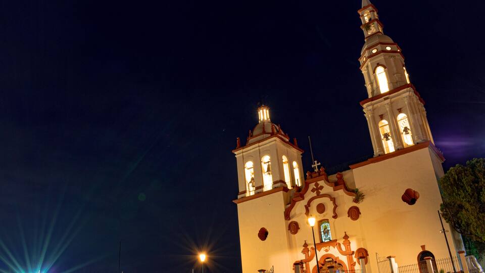 A lit church with a bell tower and a cross on top, set against a night sky.