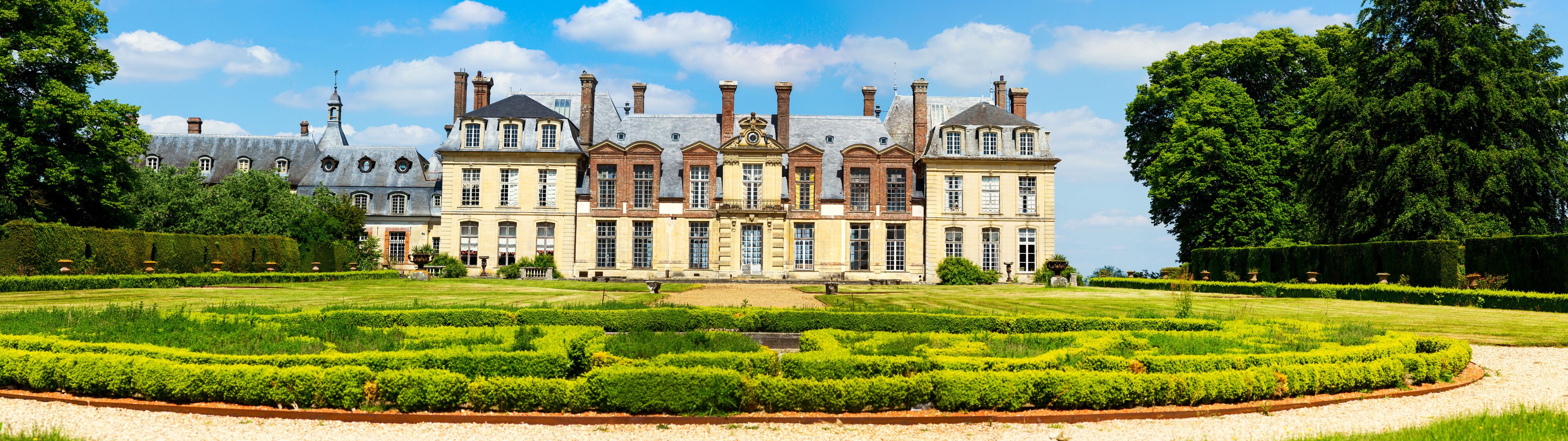 A large, historic building with a formal garden in front.