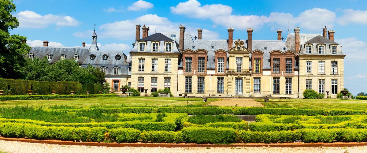A large, historic building with a formal garden in front.
