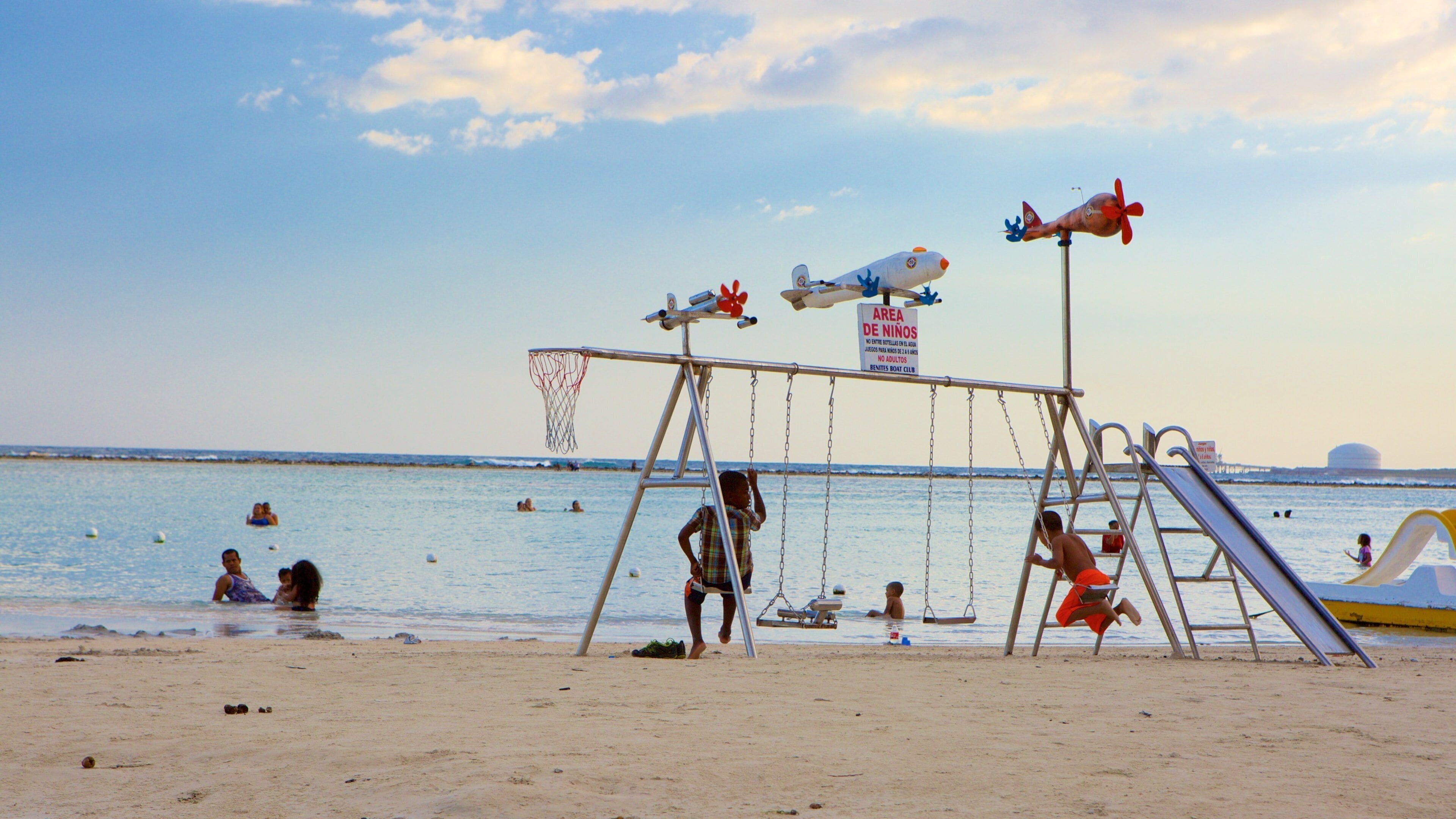 A beach with a swing set, a lifeguard tower, and a sign indicating a children's area.