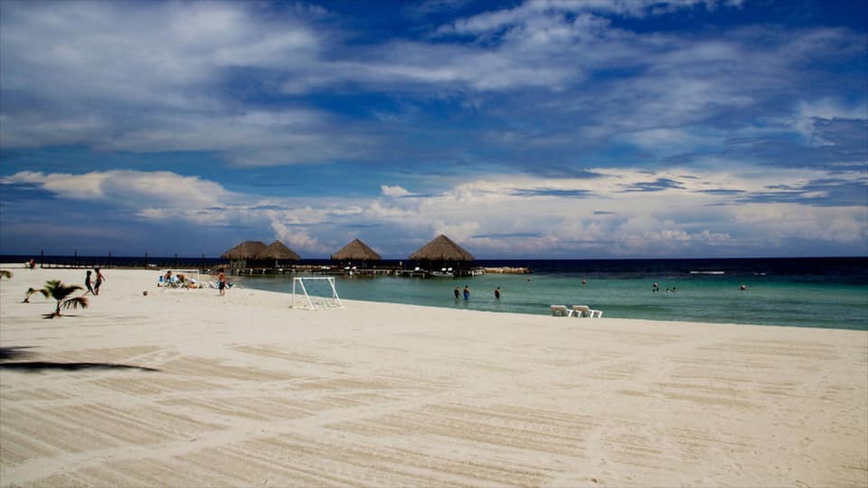 A beach with white sand, clear turquoise water, and thatched-roof huts.