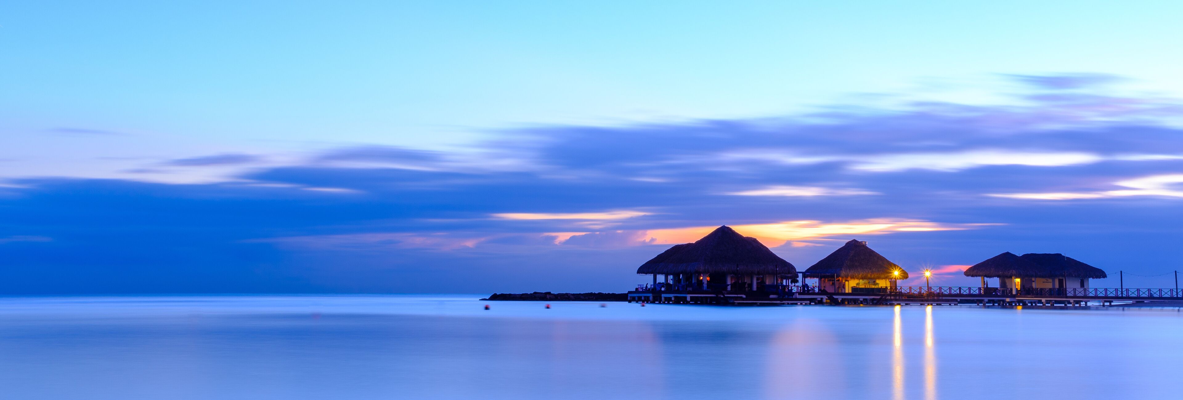 A tranquil sunset over a calm sea with overwater bungalows.