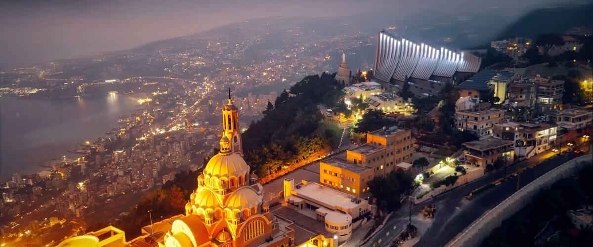 Un paisaje urbano al anochecer con una catedral destacada, un edificio moderno con un techo singular y un río en el fondo.